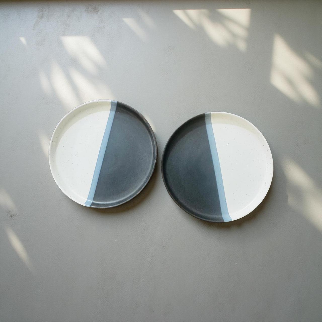 Two round ceramic coasters with a blue stripe on a light gray surface.