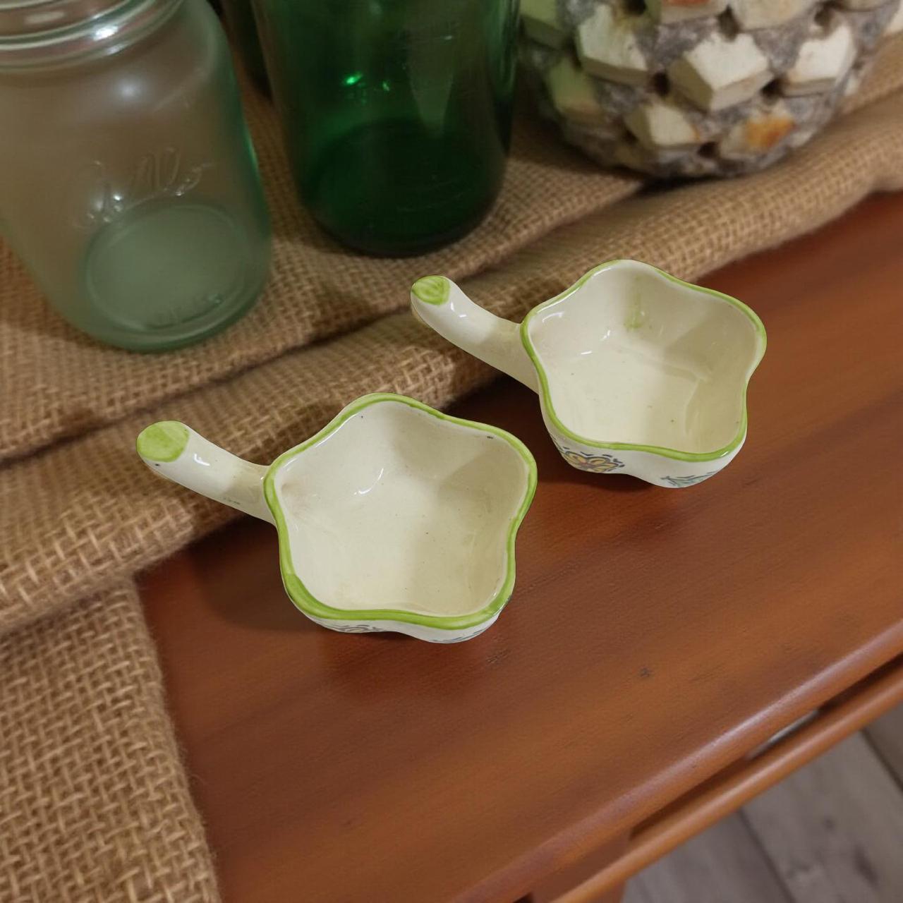 Two small ceramic planters with green handles on a wooden surface.