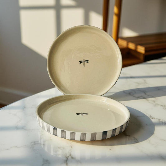 Open ceramic dish with lid featuring a dragonfly design on a marble surface.