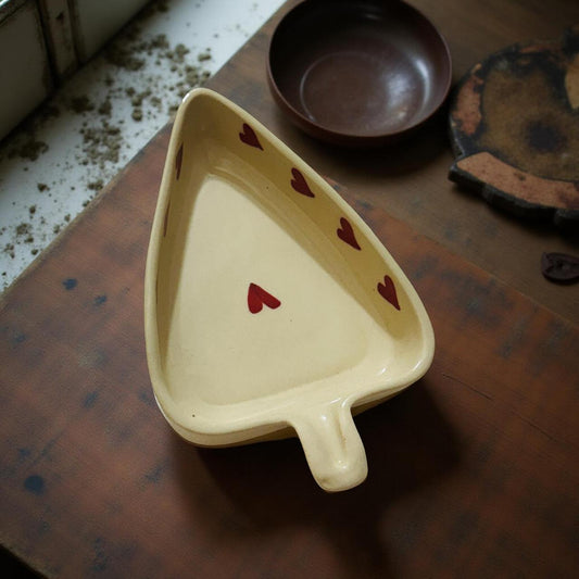 Triangular ceramic dish with red hearts on a wooden surface