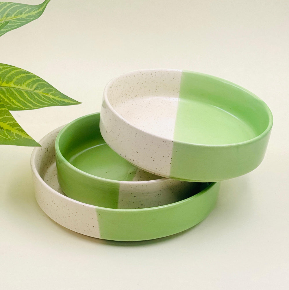 Hand-glazed stone-toned tableware with raw edges, resting on a rustic wooden counter beside herbs and bread