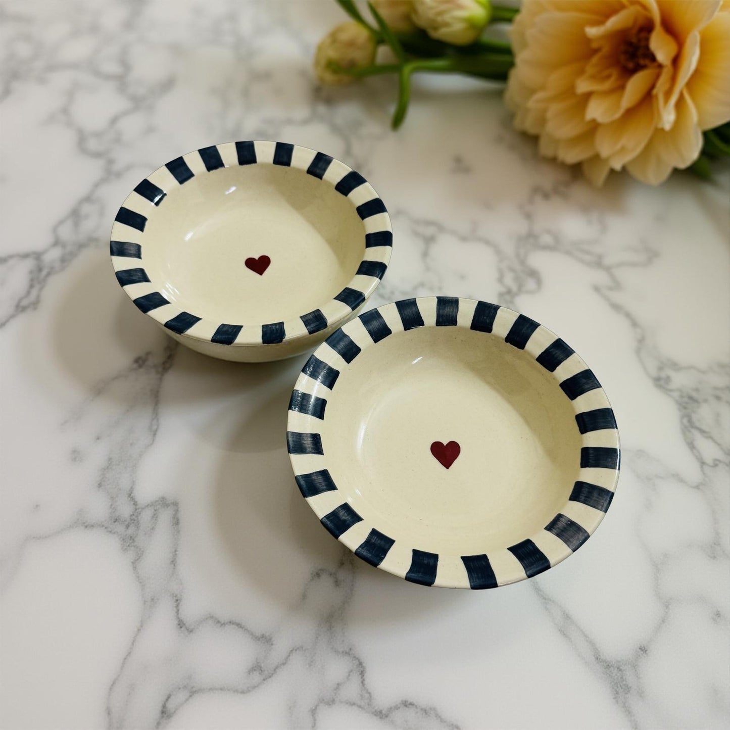 Two cream ceramic bowls with navy stripes and red heart center, placed on wooden table