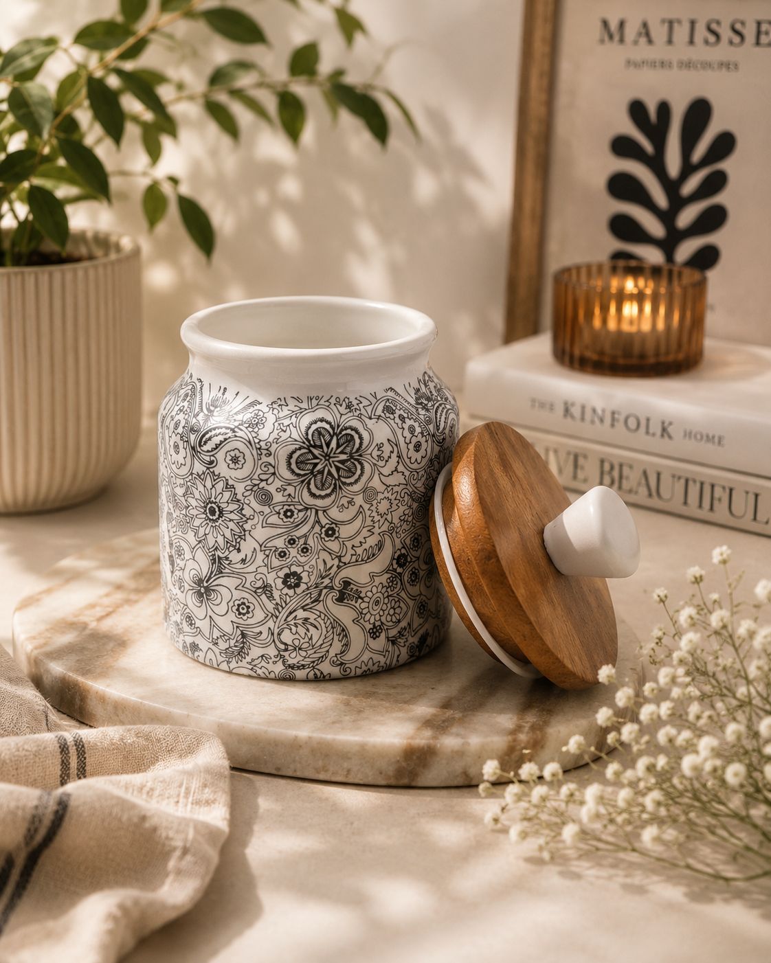 Decorative candle holder with black and white pattern on a wooden surface with books and plants in the background.