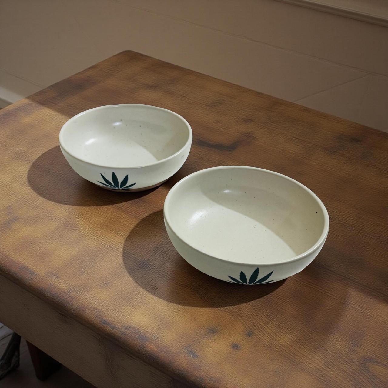 Two ceramic bowls with green leaf patterns on a wooden surface.