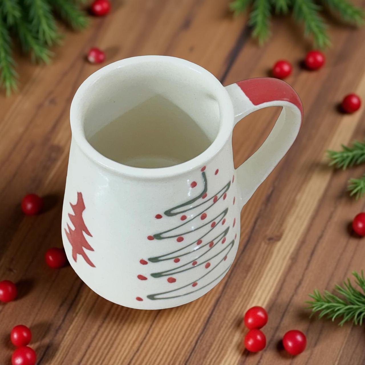 White mug with red handle and festive design on a wooden surface with red berries and greenery.