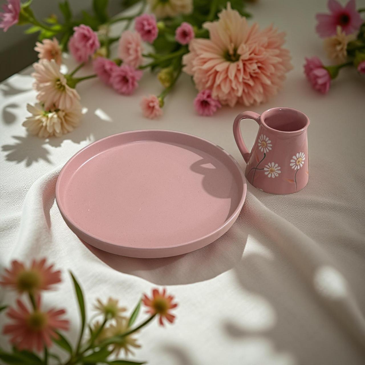 Handcrafted blush pink ceramic plate with floral mug on white fabric, surrounded by pastel flowers – ideal Rakhi gift set.