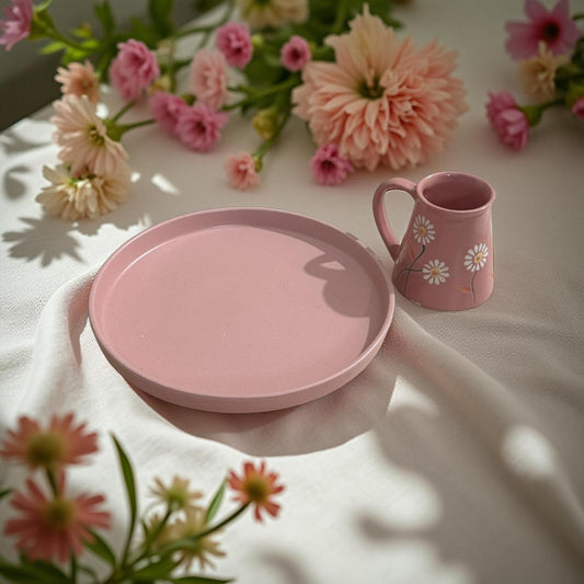 Handcrafted blush pink ceramic plate with floral mug on white fabric, surrounded by pastel flowers – ideal Rakhi gift set.