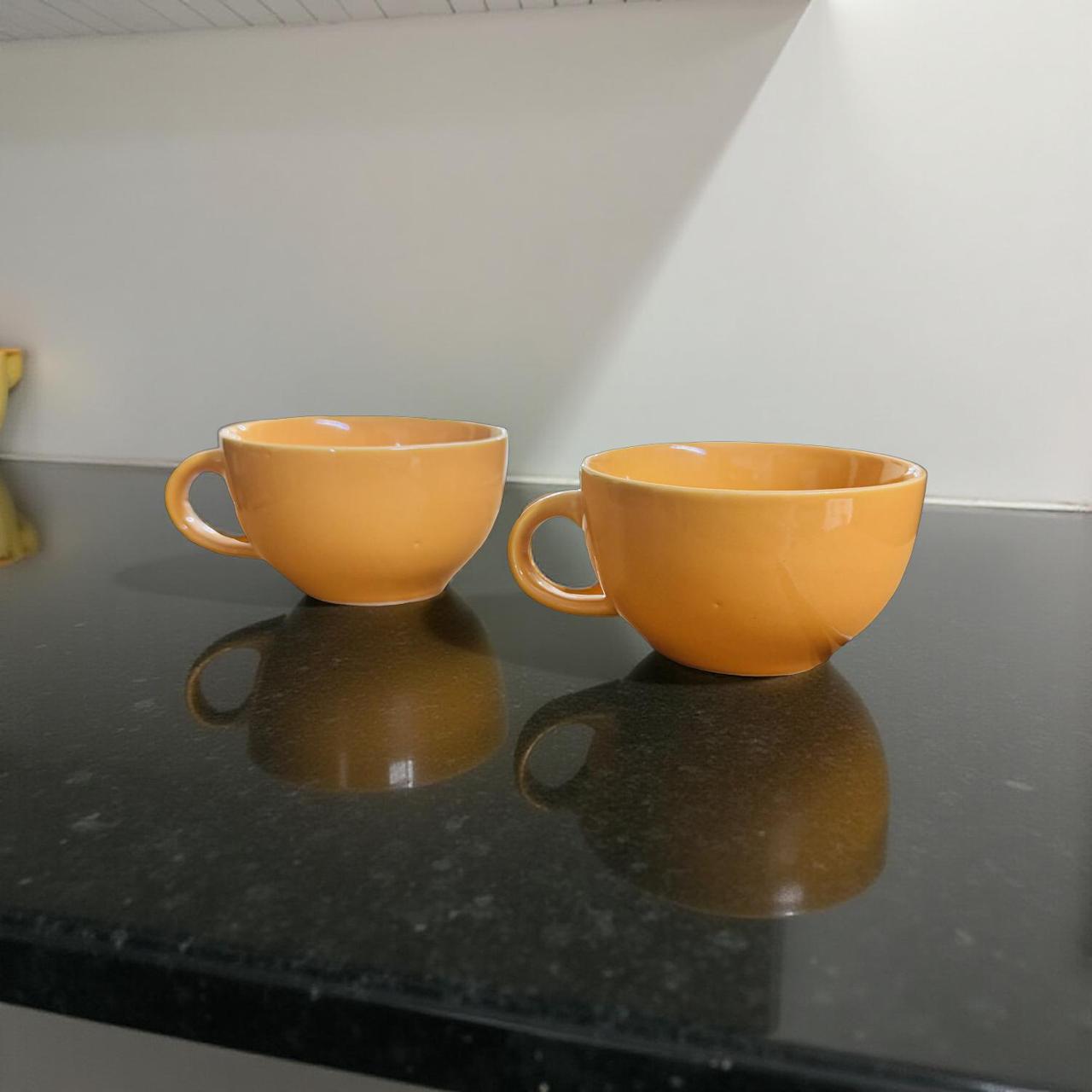 Two yellow cups on a reflective black surface with a neutral background