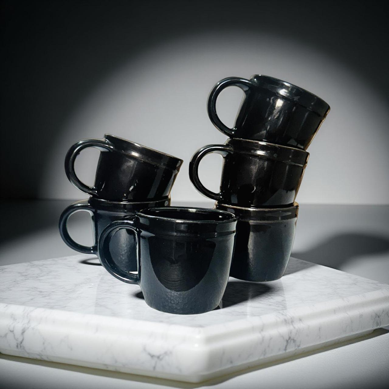 Stack of black ceramic mugs on a marble surface with a dark background