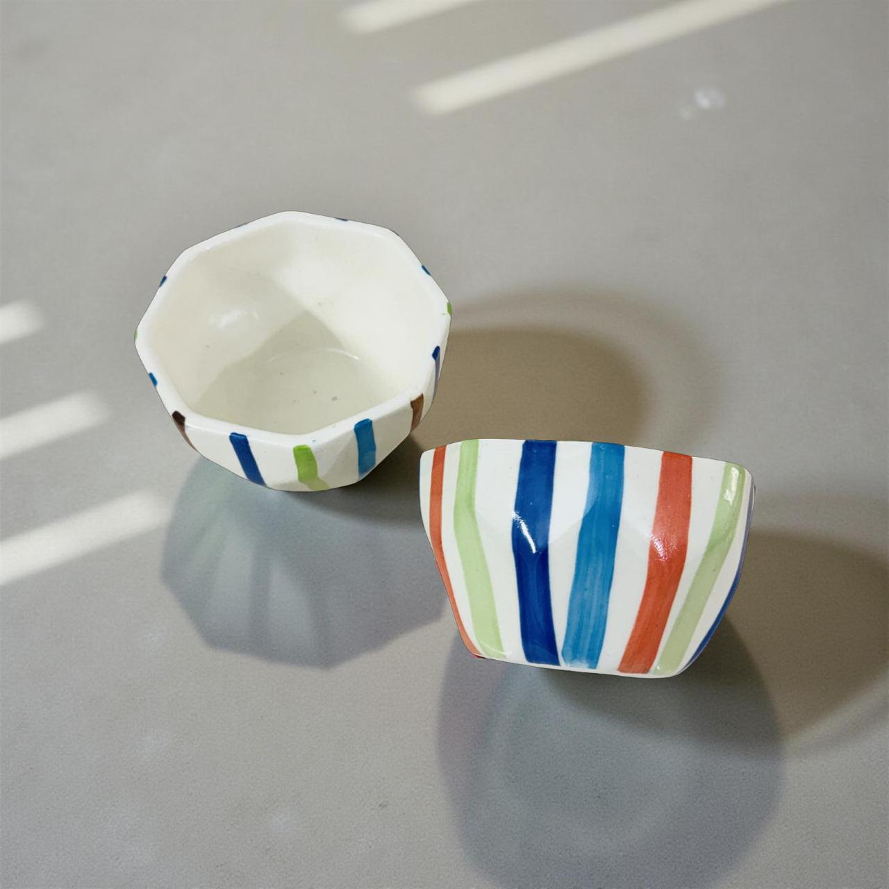 Two ceramic bowls with colorful striped patterns on a gray surface.