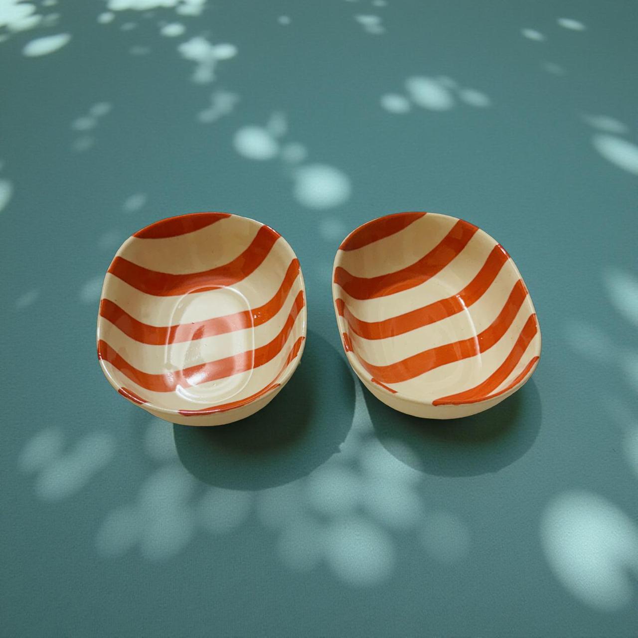 Two ceramic bowls with orange and white striped patterns on a green surface with leaf shadows.