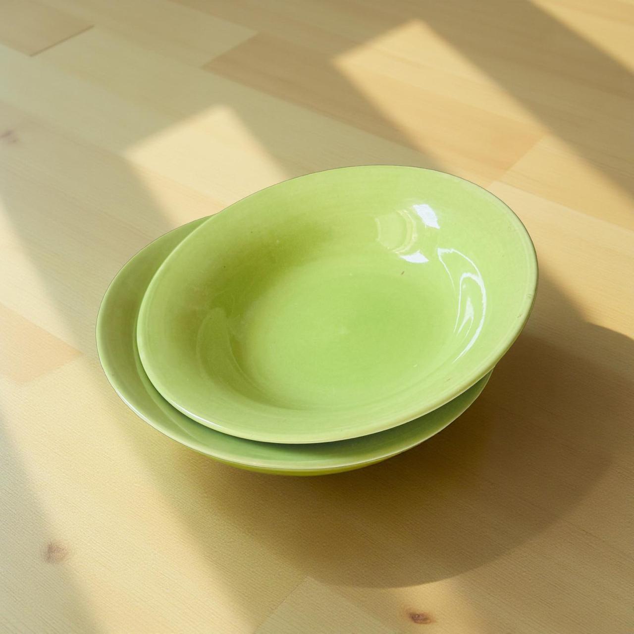 Two green ceramic bowls stacked on a wooden surface with sunlight casting shadows.