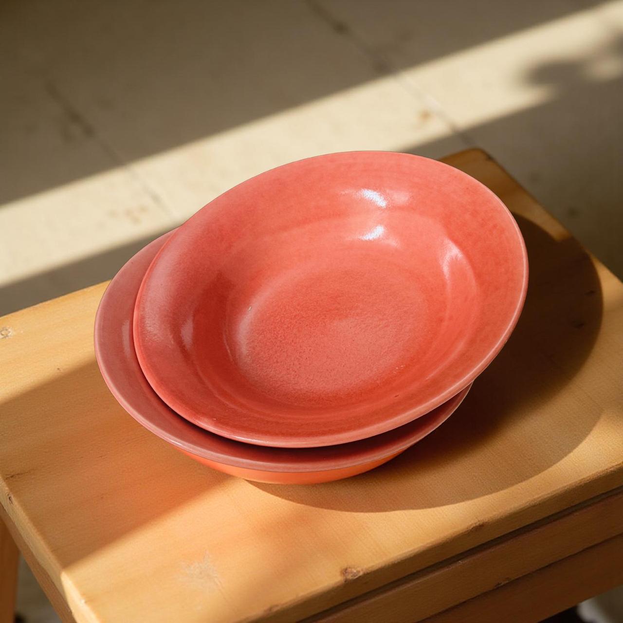 Stack of pink ceramic bowls on a wooden surface with sunlight casting shadows.