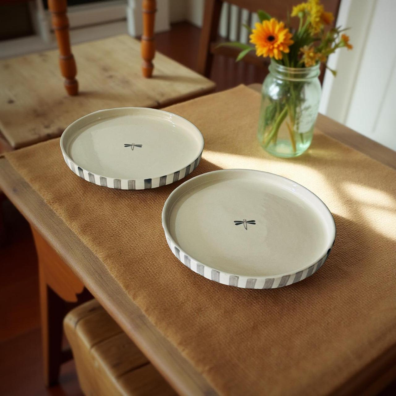 Two ceramic plates with decorative edges on a wooden table with a vase of flowers.