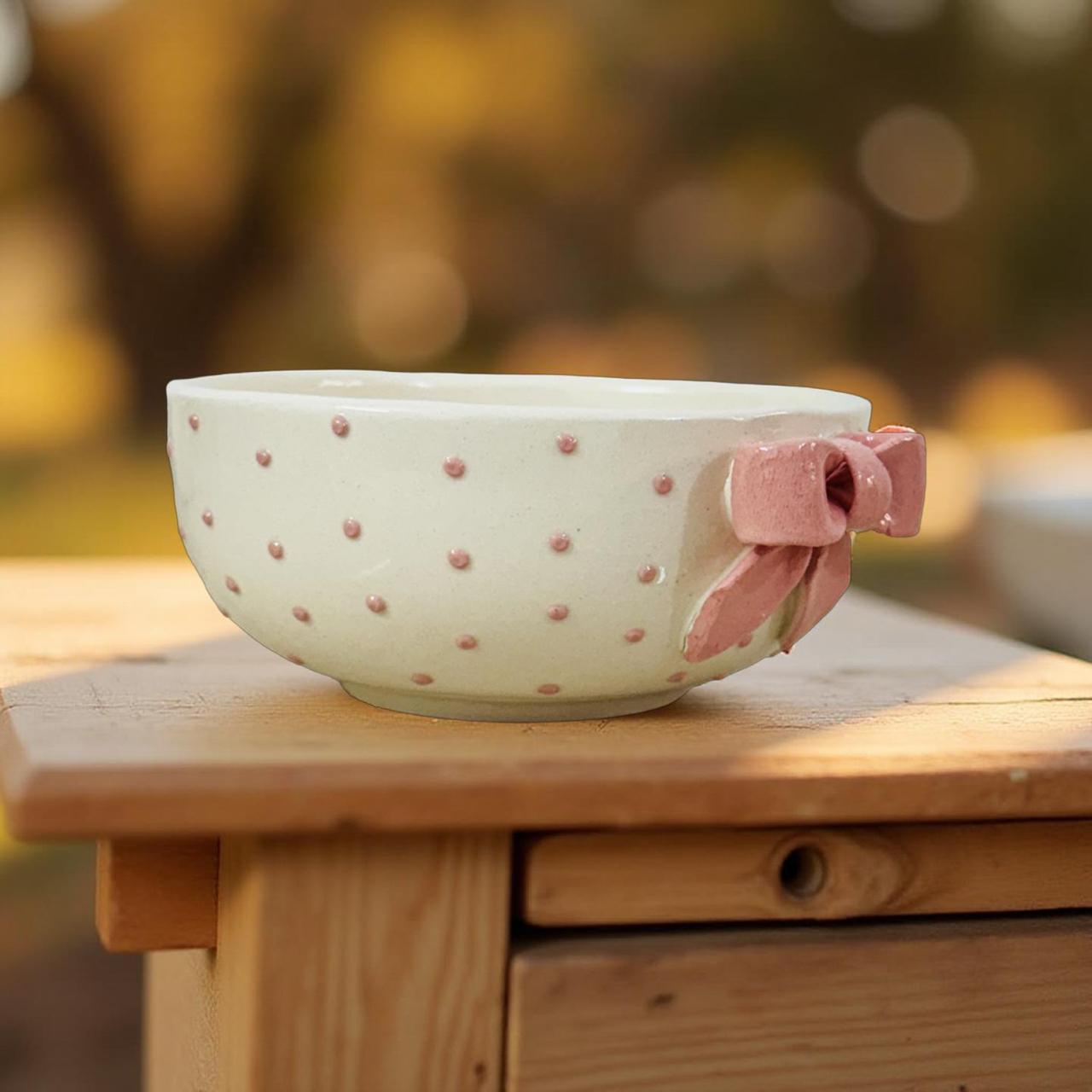 Ceramic bowl with pink polka dots and a pink ribbon on a wooden surface with a blurred natural background
