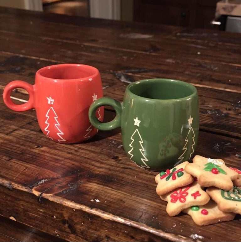 Two Christmas-themed mugs on a wooden surface with cookies.