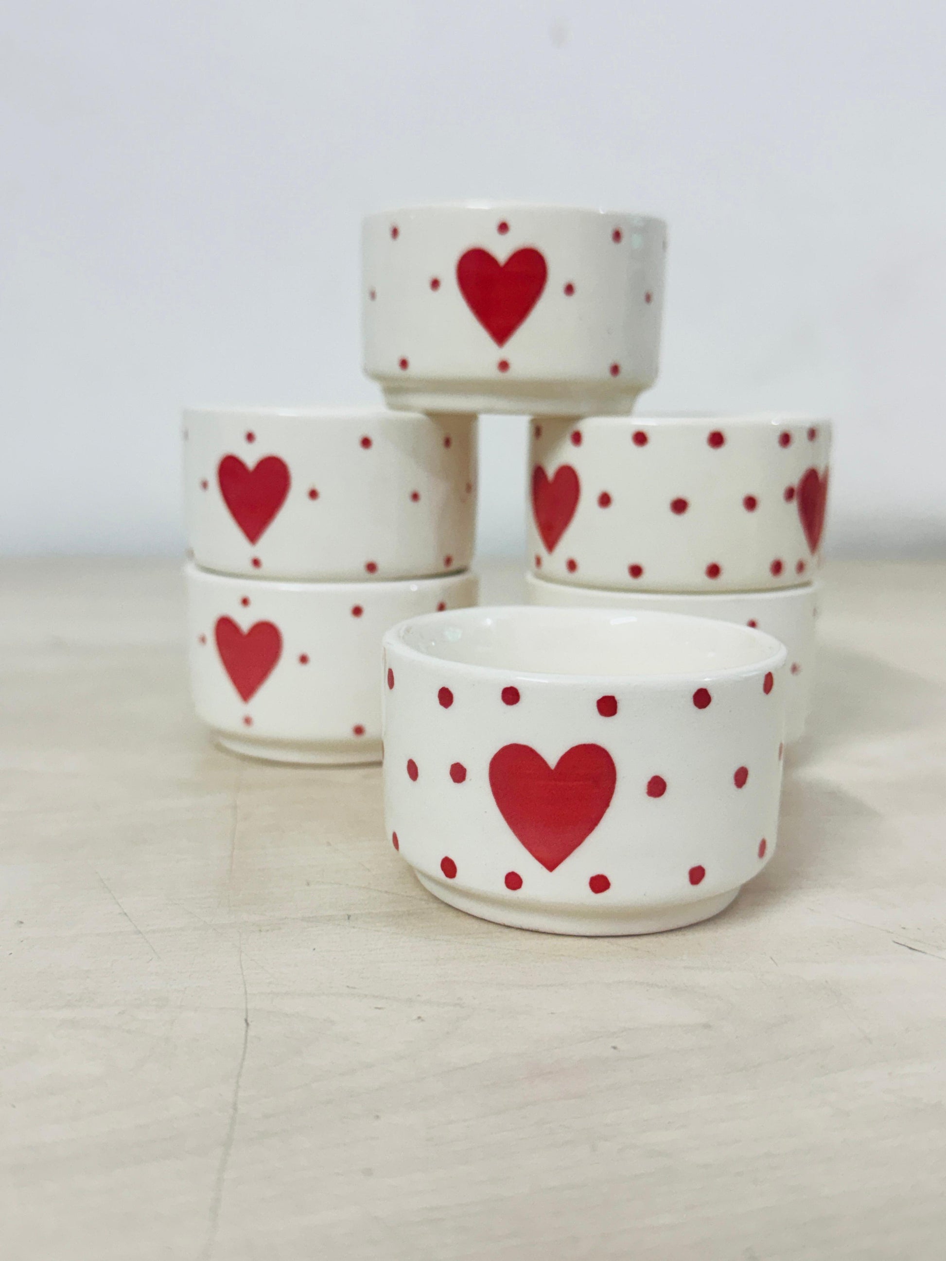 Set of ceramic bowls with red heart and polka dot patterns on a light background