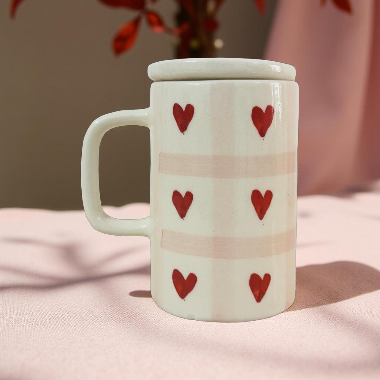 White mug with red heart patterns on a pink surface