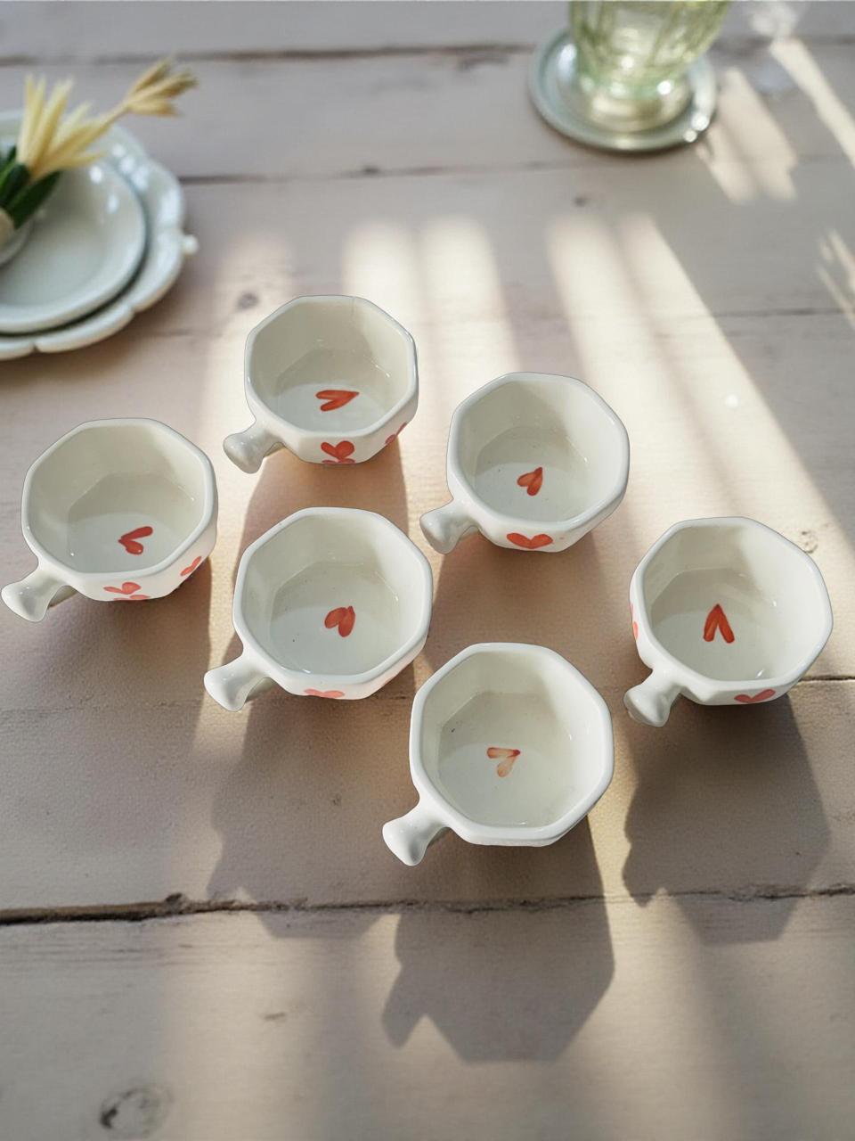 six white chutney bowl with handle are kept on a wooden table with flowers and plates