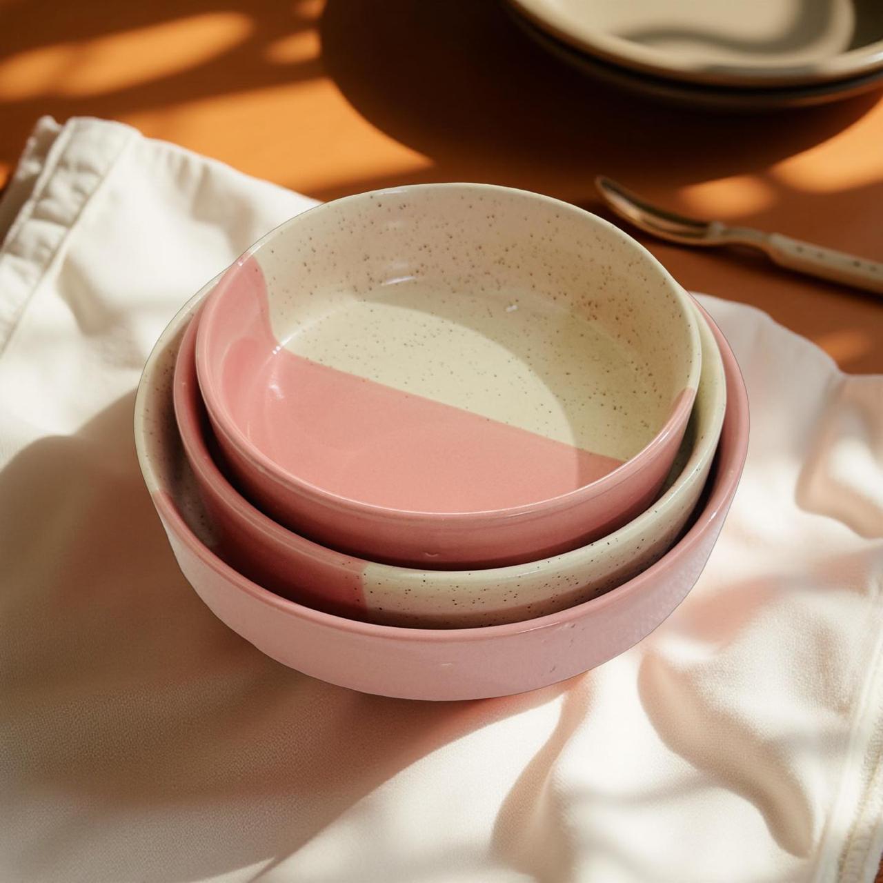 Stack of pink and beige ceramic bowls on a light fabric surface.