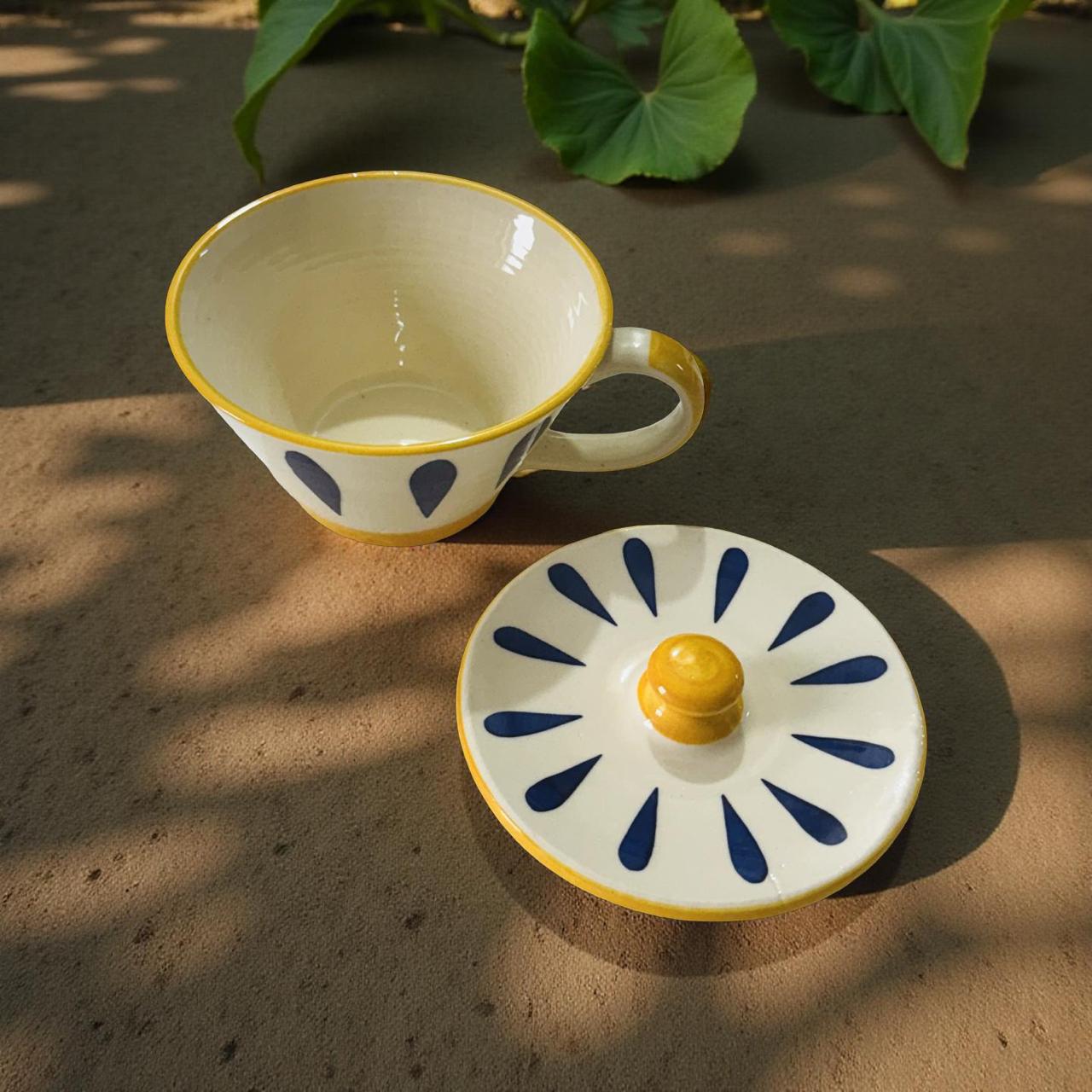 Ceramic cup and lid with blue and yellow patterns on a textured surface.