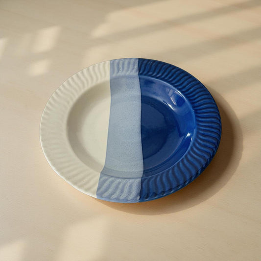 half white and  blue ceramic plates, one white and one blue, on a beige surface.