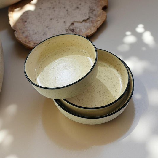 Two ceramic bowls stacked on a light surface with bread in the background