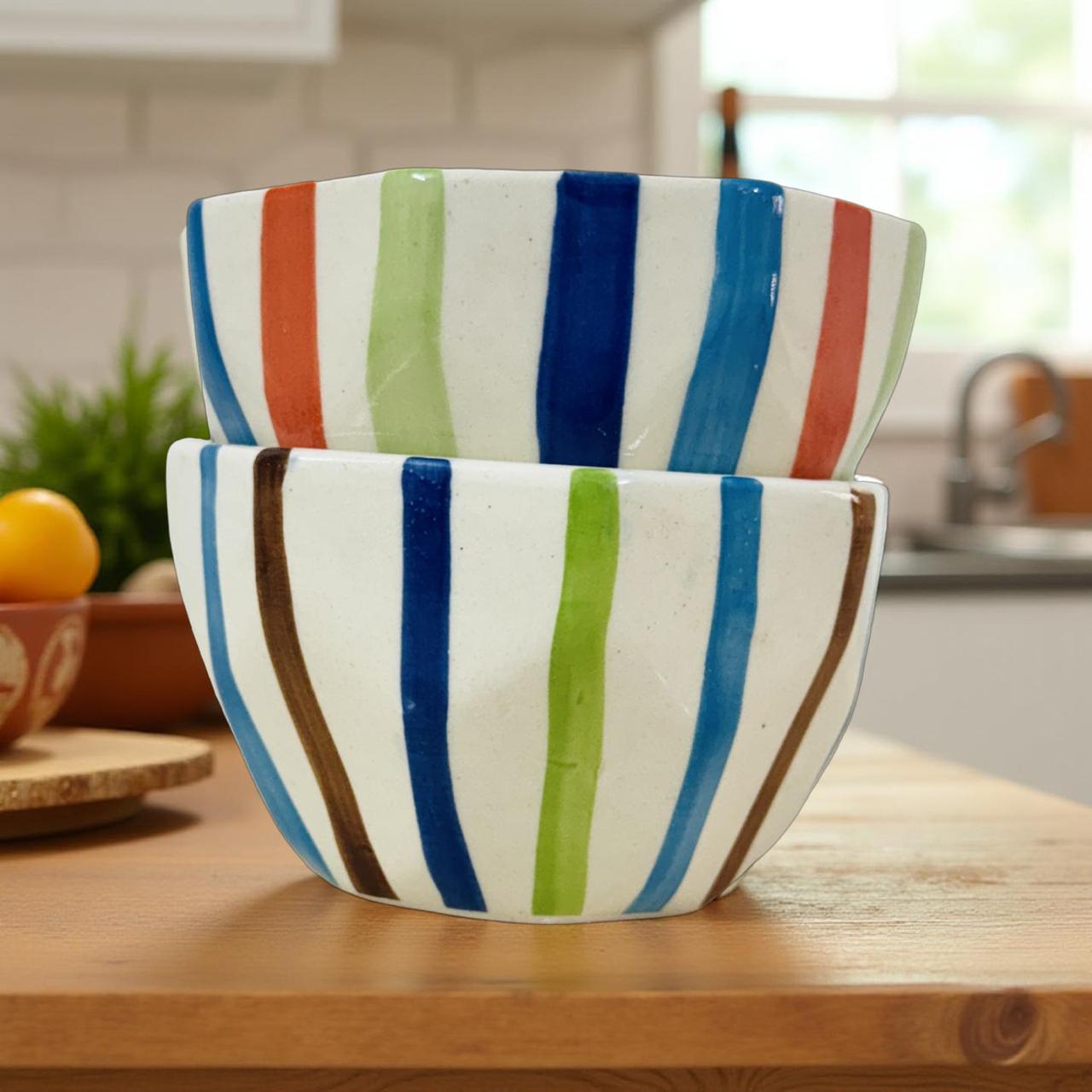 Two ceramic bowls with colorful stripes on a wooden surface in a kitchen.