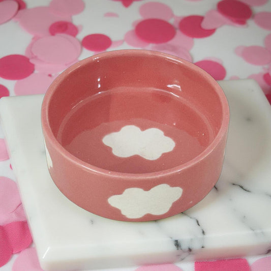 Pink pet bowl with paw prints on a marble surface and pink polka dot background