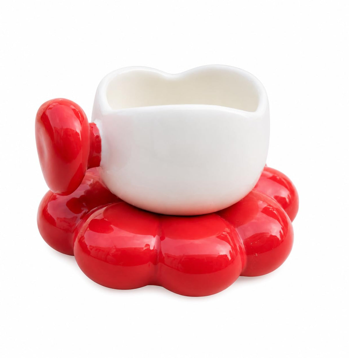 A glossy white ceramic cup with a heart-shaped rim, resting on a bright red flower-shaped saucer, isolated on a white background.