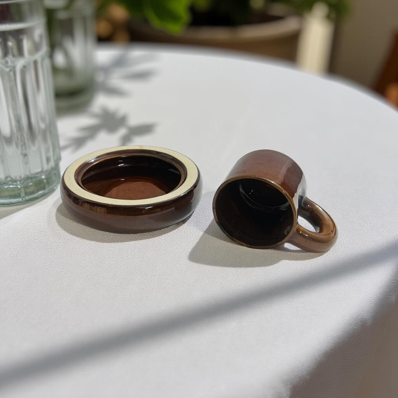 Brown ceramic mug and coaster on a white surface with a blurred background