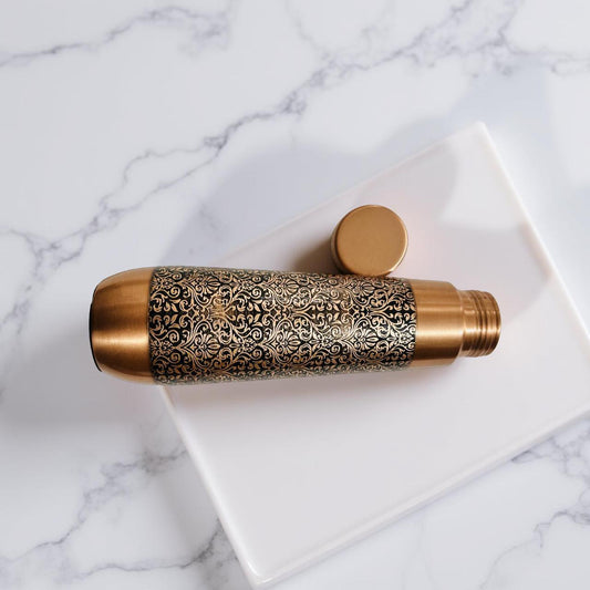 Decorative brass water bottle with intricate patterns on a marble surface