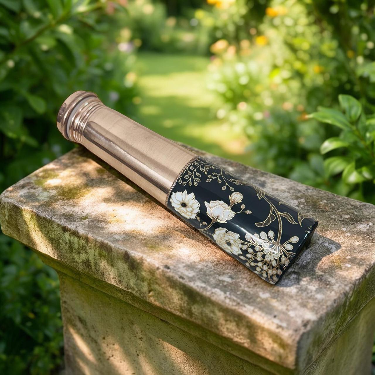 Decorative copper bottle with floral design on a stone surface in a garden setting