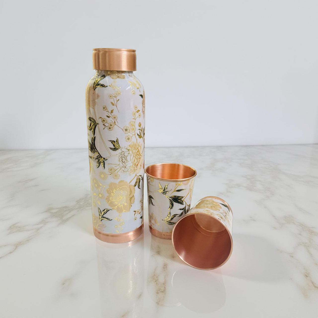 Floral-patterned water bottle and copper cups on a marble surface