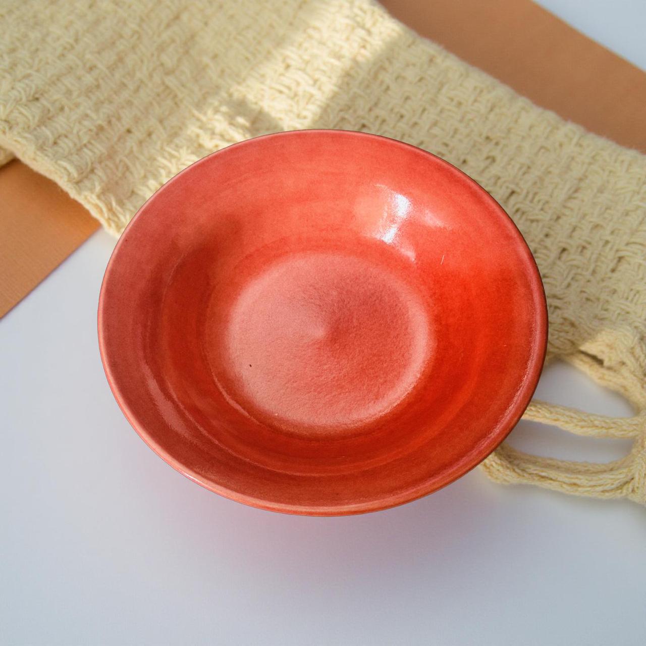 Red ceramic bowl on a white surface with a beige woven mat in the background