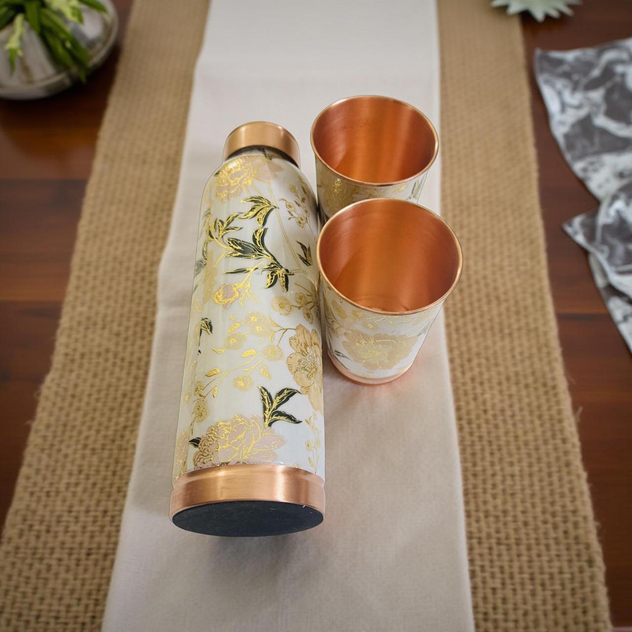 Floral-patterned water bottle and copper cups on a table runner