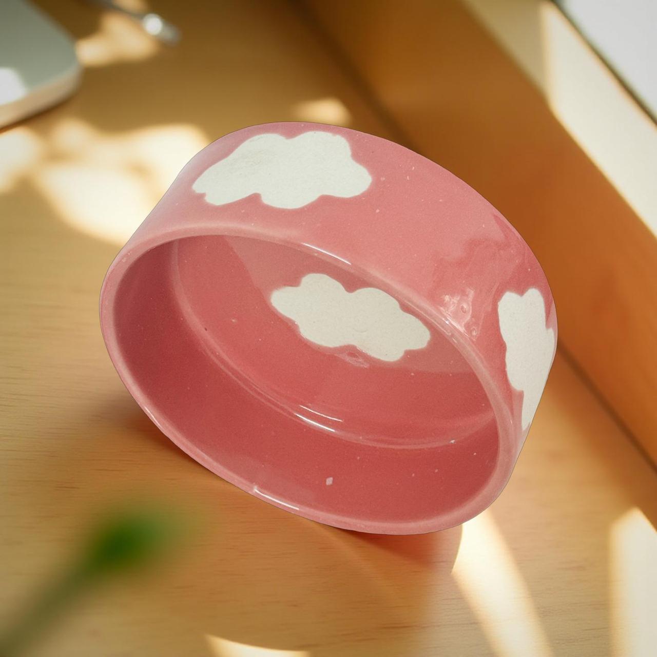 Pink pet bowl with cloud designs on a wooden surface