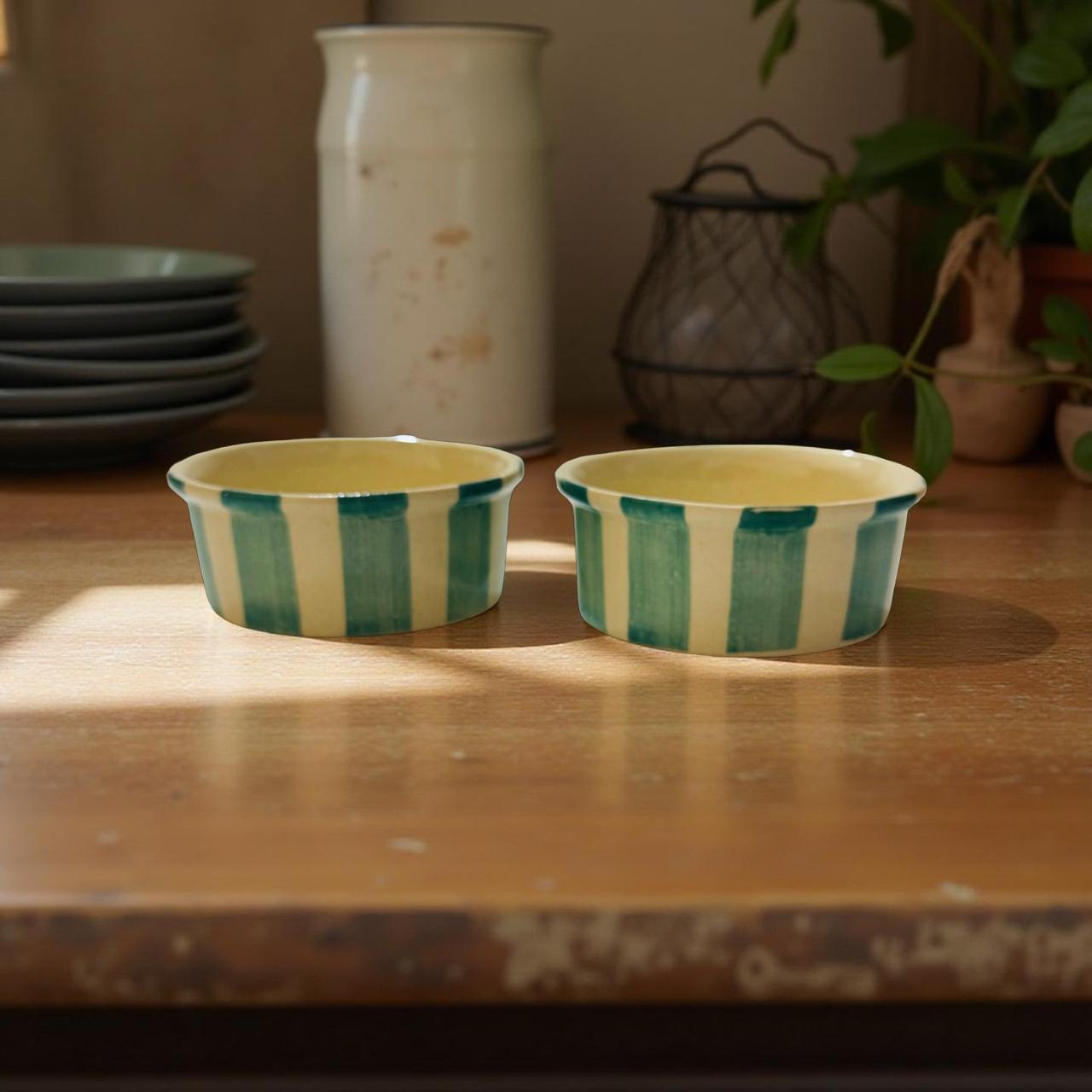 Two ceramic bowls with green and white stripes on a wooden surface.