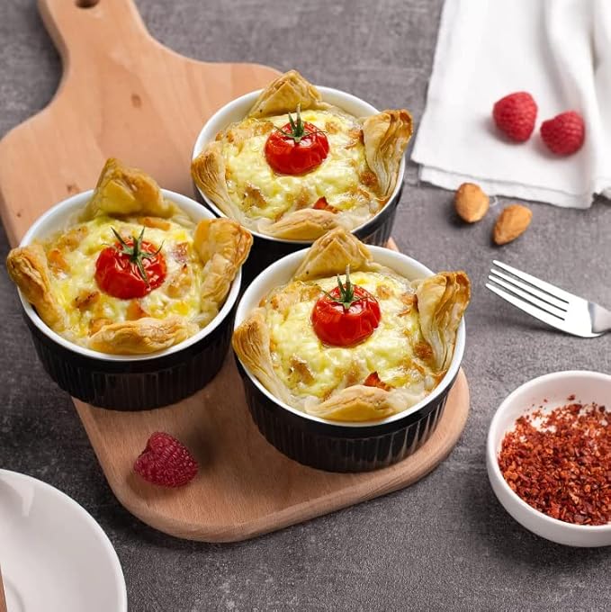 Three small baked dishes with cheese and tomatoes on a wooden board with raspberries and a fork.