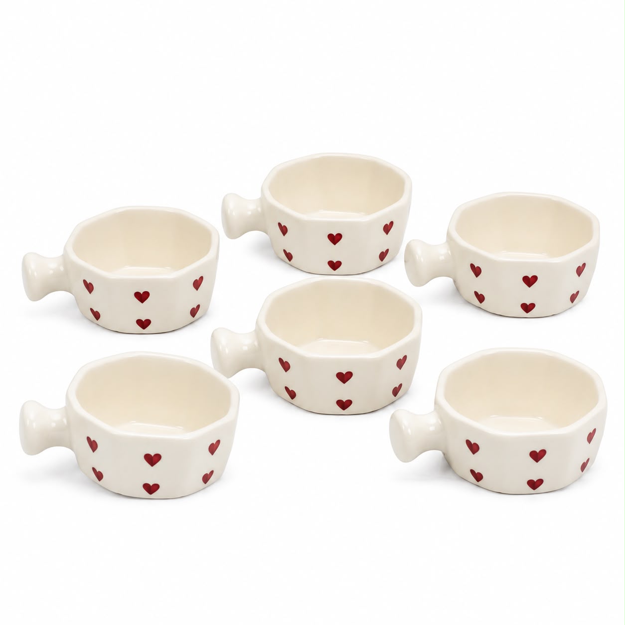 Six small white ceramic cups with handles, decorated with small red hearts, arranged on a white background.