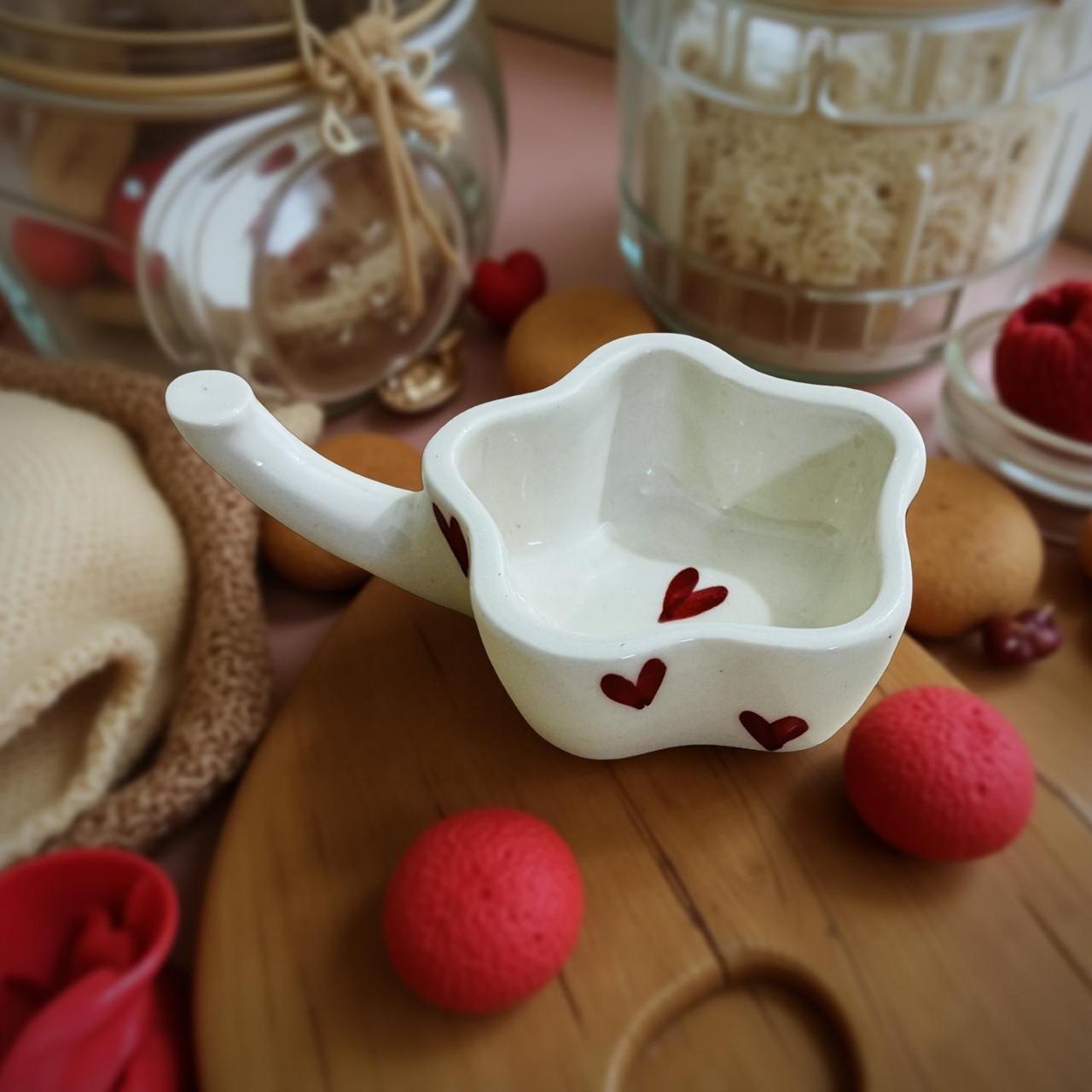 White ceramic bowls with red heart designs on a wooden surface with red balls and jars in the background.