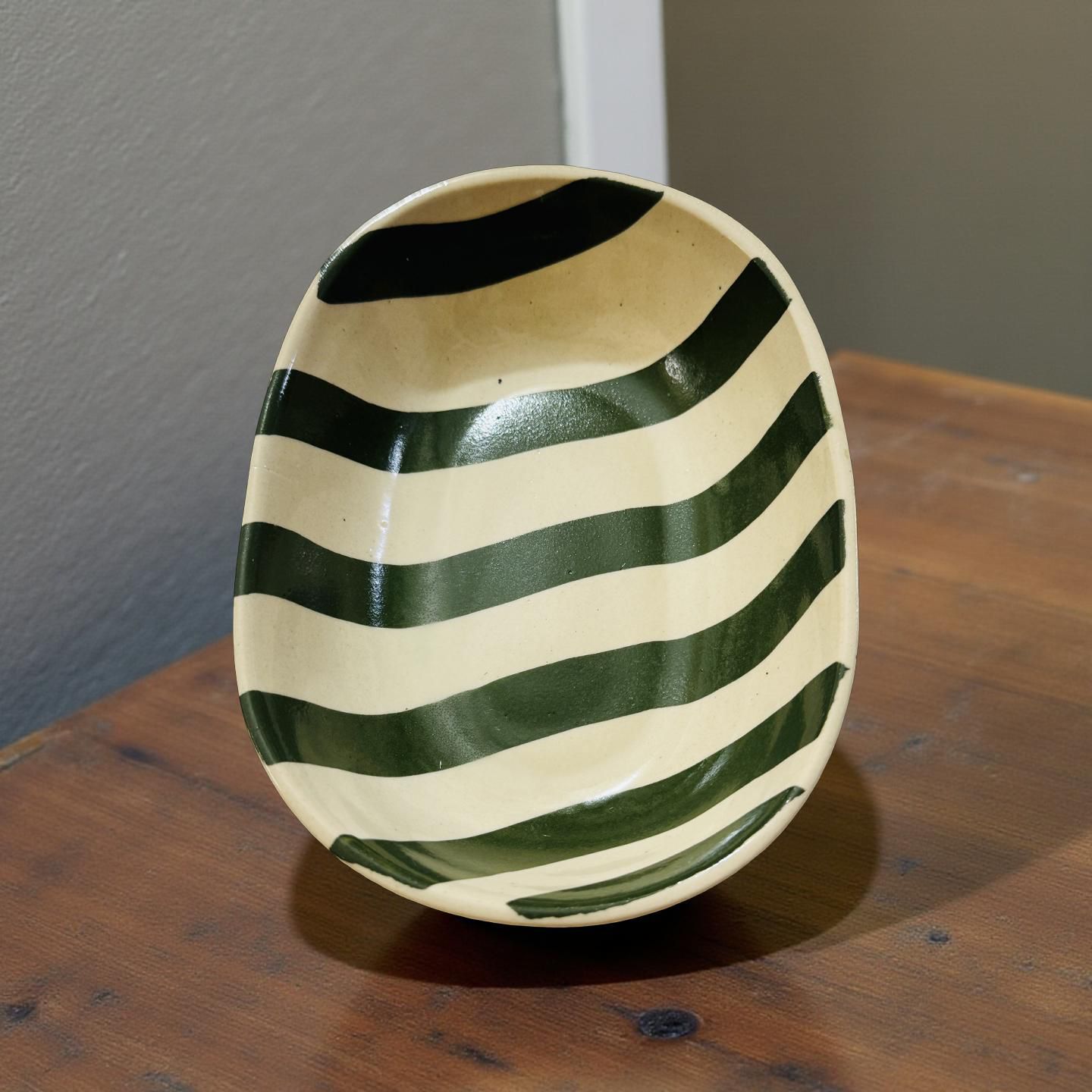 Ceramic bowl with green and white stripes on a wooden surface