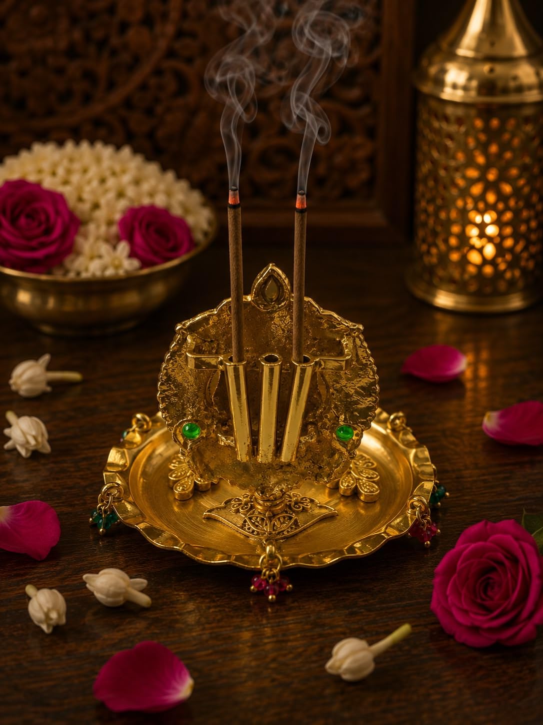An ornate gold-toned brass incense holder with two smoking incense sticks, styled on a dark wooden table with rose petals, white and pink roses, and a brass lantern in the background.