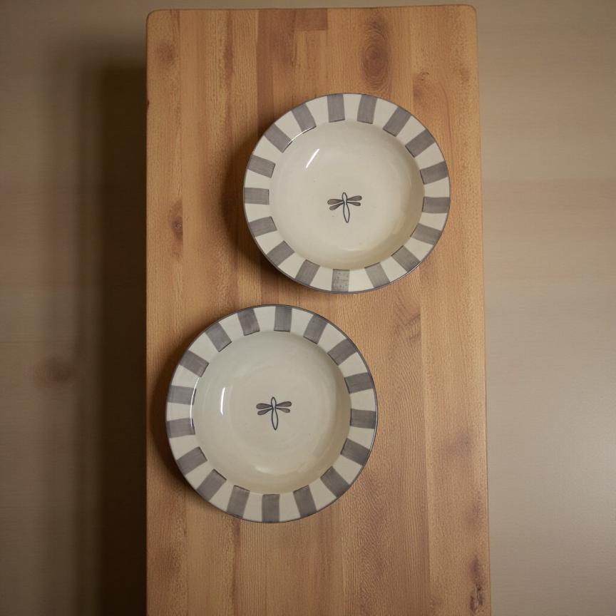 Two ceramic plates with gray stripes and a dragonfly design on a wooden surface.