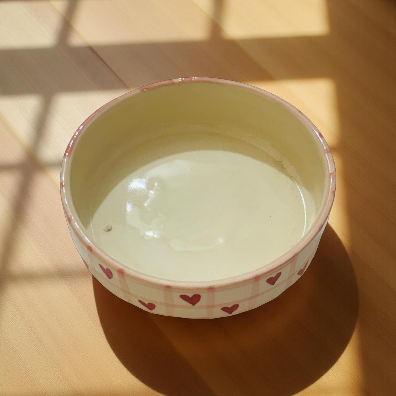 Small ceramic bowl with pink rim and heart patterns on a wooden surface