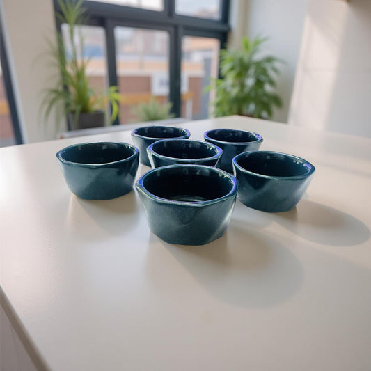 Set of six dark blue ceramic bowls on a light surface with a blurred indoor background