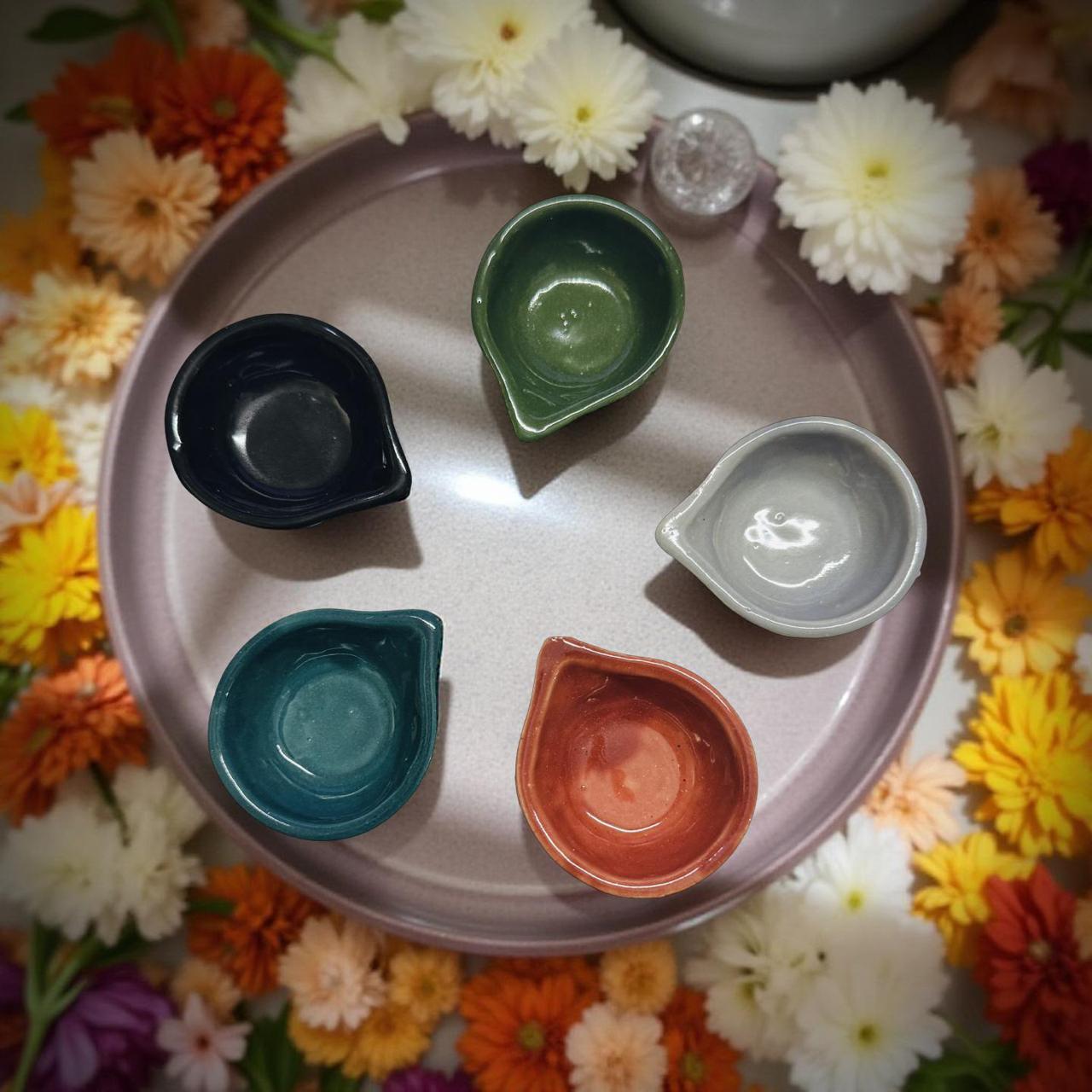 Five small bowls of different colors on a round tray with flowers around it.