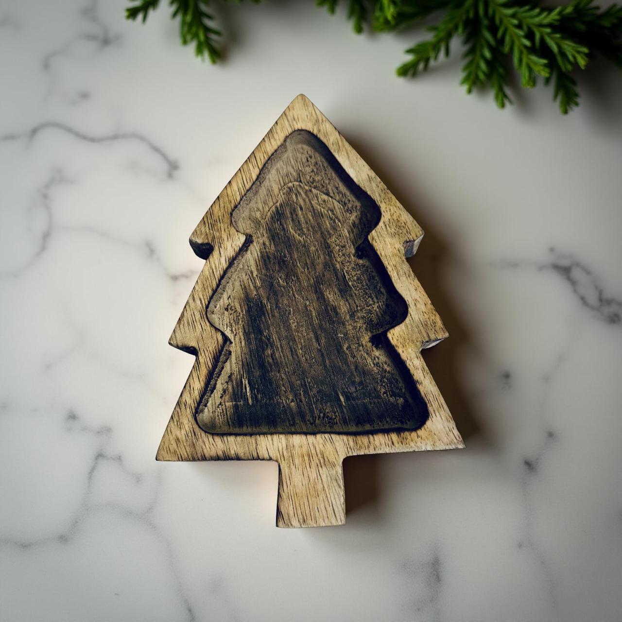 Wooden Christmas tree ornament on a marble surface with greenery in the background