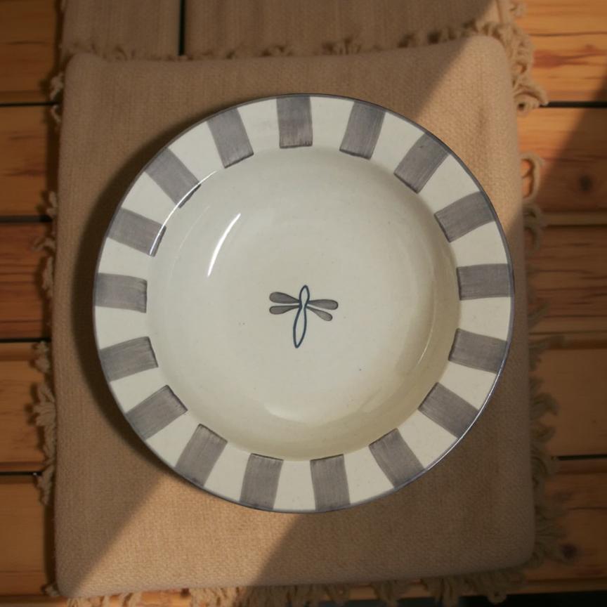 White plate with gray stripes and a dragonfly design on a brown fabric background