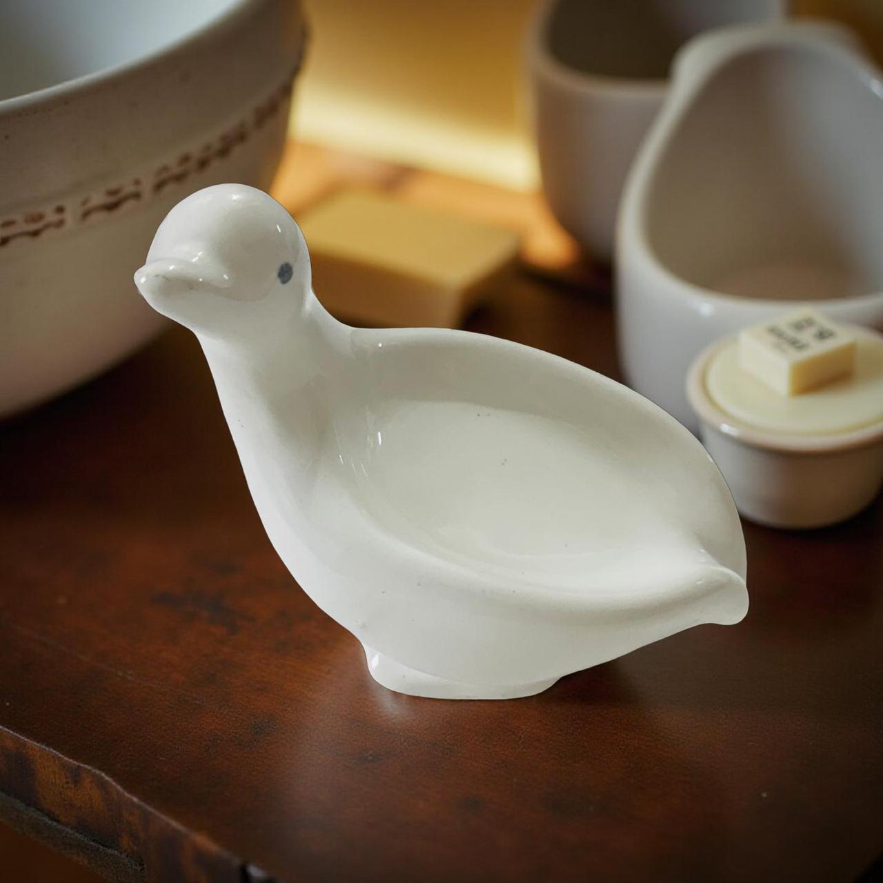 White ceramic duck-shaped dish on a wooden surface with other kitchen items in the background.